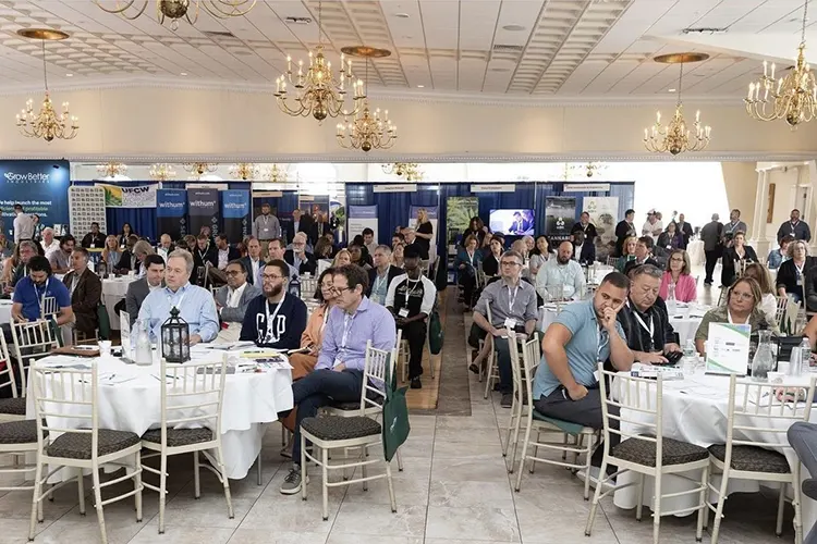 Seated guests wearing lanyards attend a presentation at a trade show