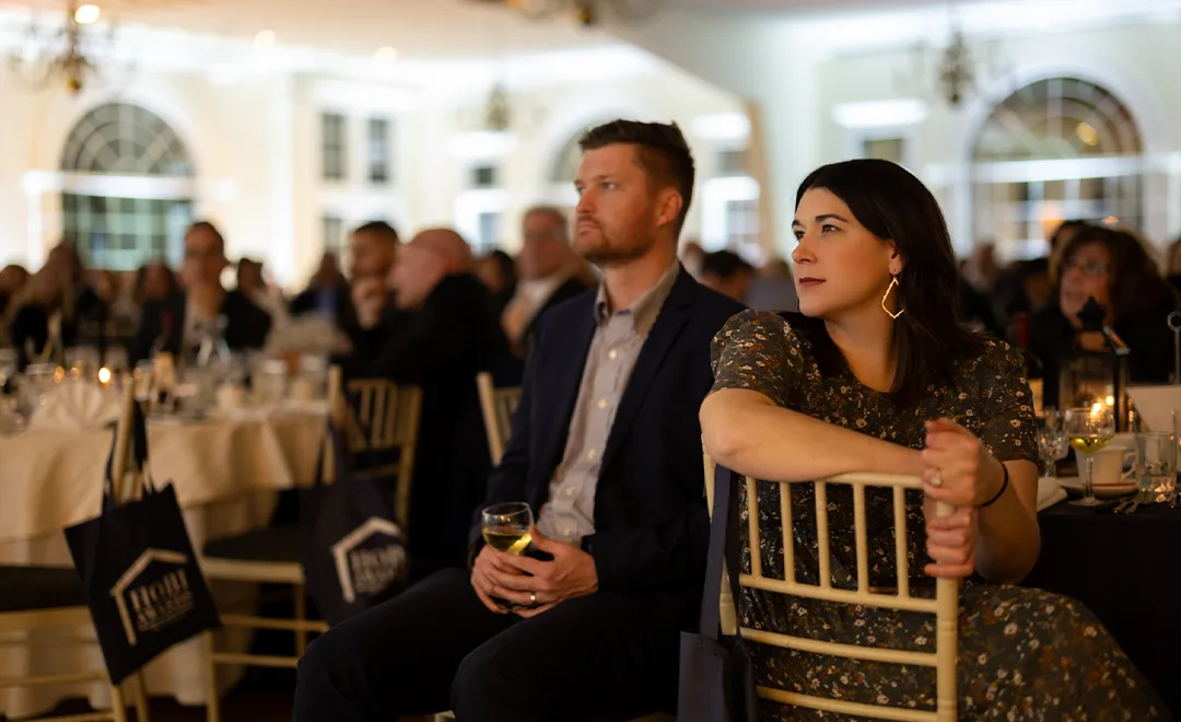 Man and woman in formal wear listen intently to the speaker at an event
