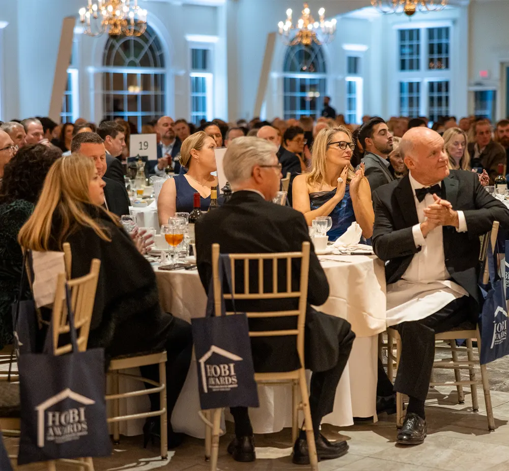 Seated guests in formal attire applaud the speaker at a corporate awards event